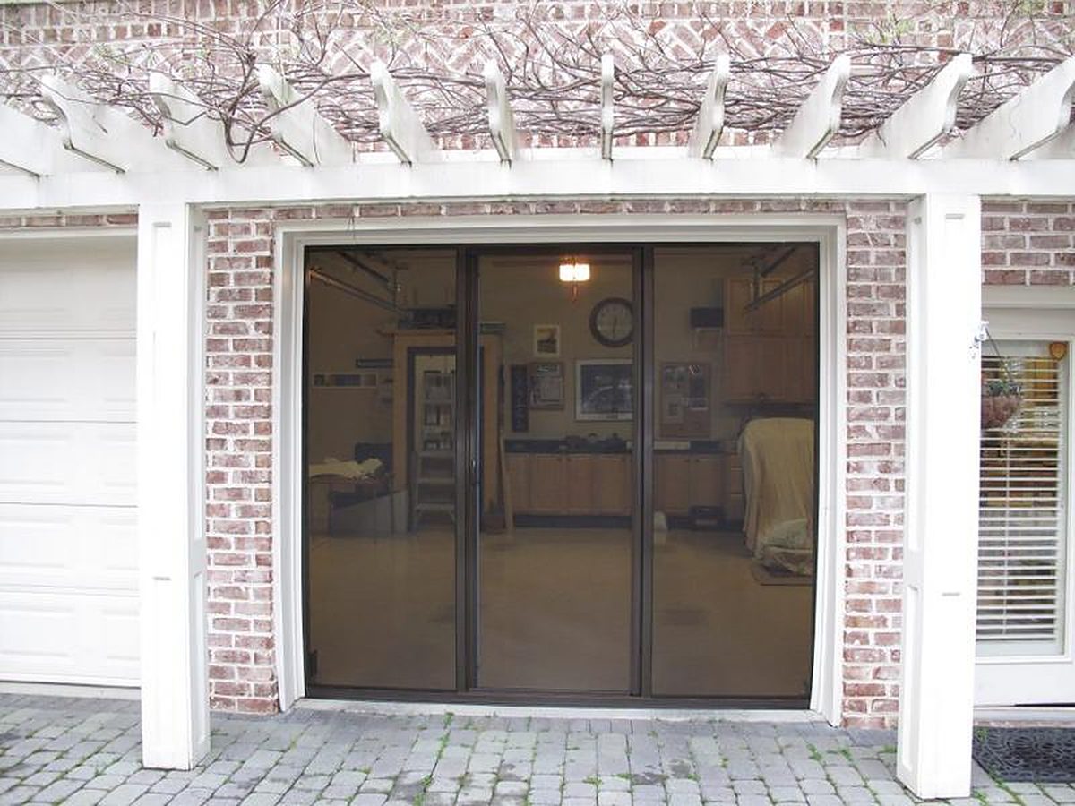 Brown-framed Lifestyle garage screen with charcoal mesh on a single brick garage under a pergola