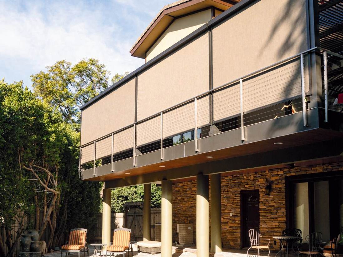 Tan motorized privacy screens along an upstairs balcony with a stone patio below