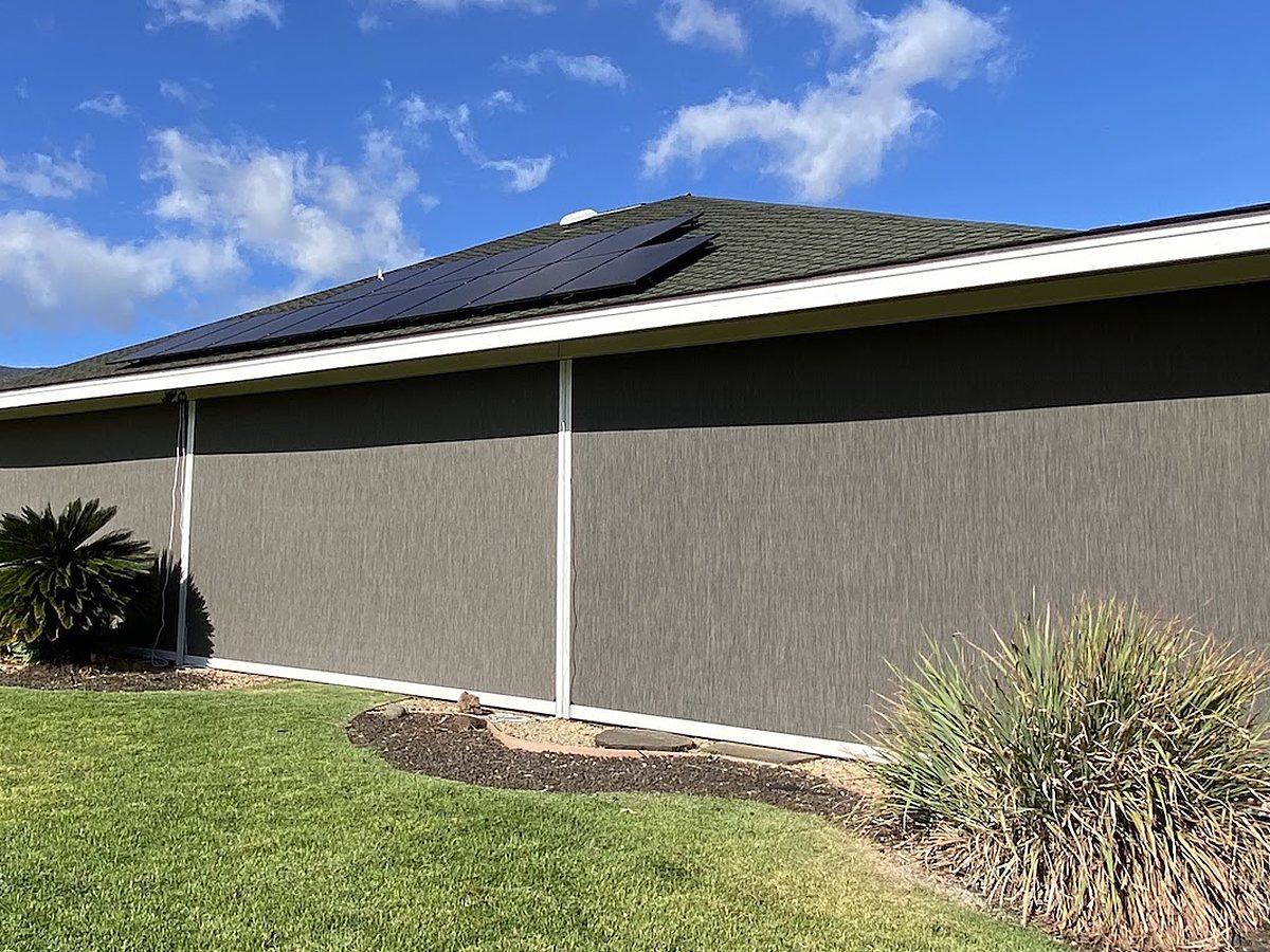 Long run of gray motorized patio screens lowered along the side of a covered outdoor room
