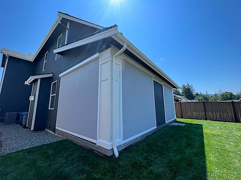Two white motorized screens enclosing the corner of a covered patio on a dark-sided house