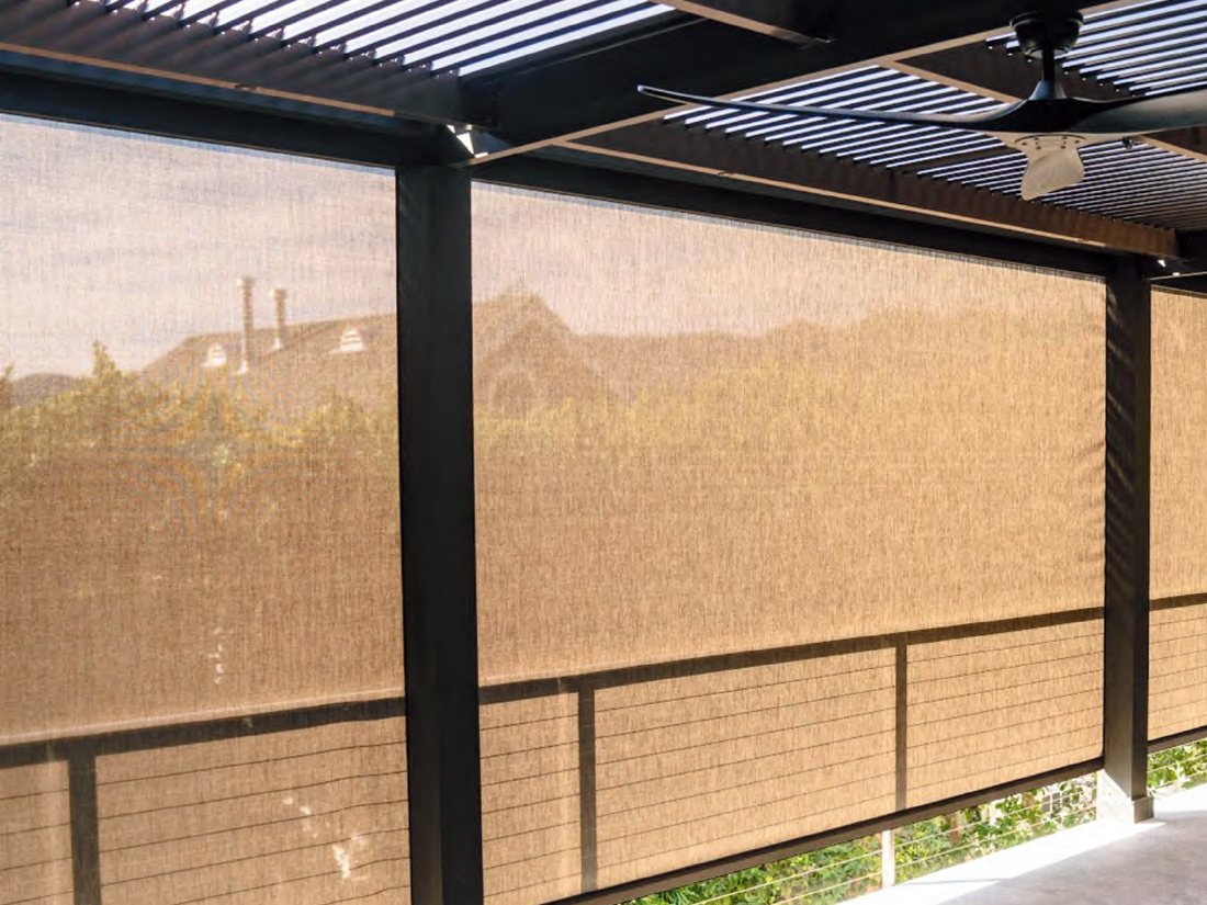 Tan fabric motorized screens between the posts of a louvered pergola