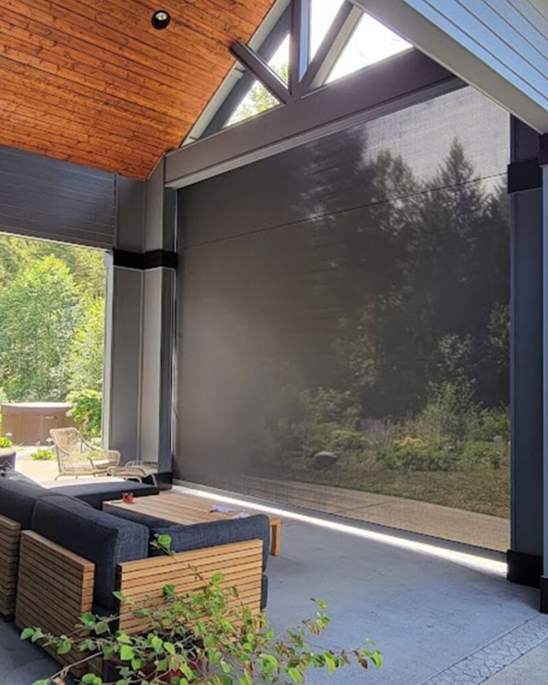 Motorized screen lowered across a covered outdoor lounge with a wood ceiling and sectional sofa